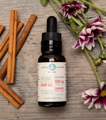 Image of Auntie Dolores 1500 mg Organic Full Spectrum Hemp CBD Oil surrounded by cinnamon sticks and flowers