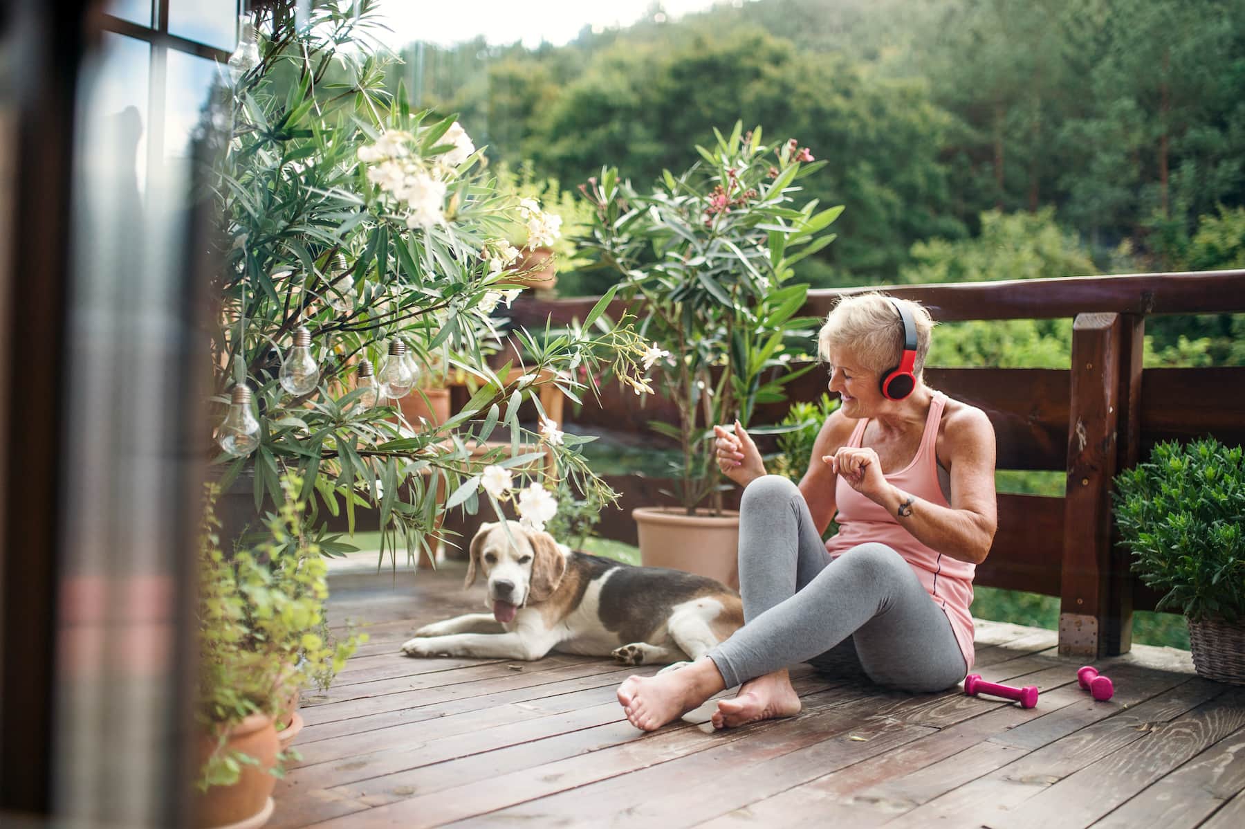 A mature woman with headphones outdoors on a terrace resting with senior dog after exercise
