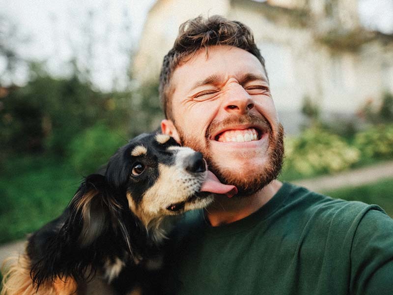 A smiling man in a green shirt cuddling with his rescue dog